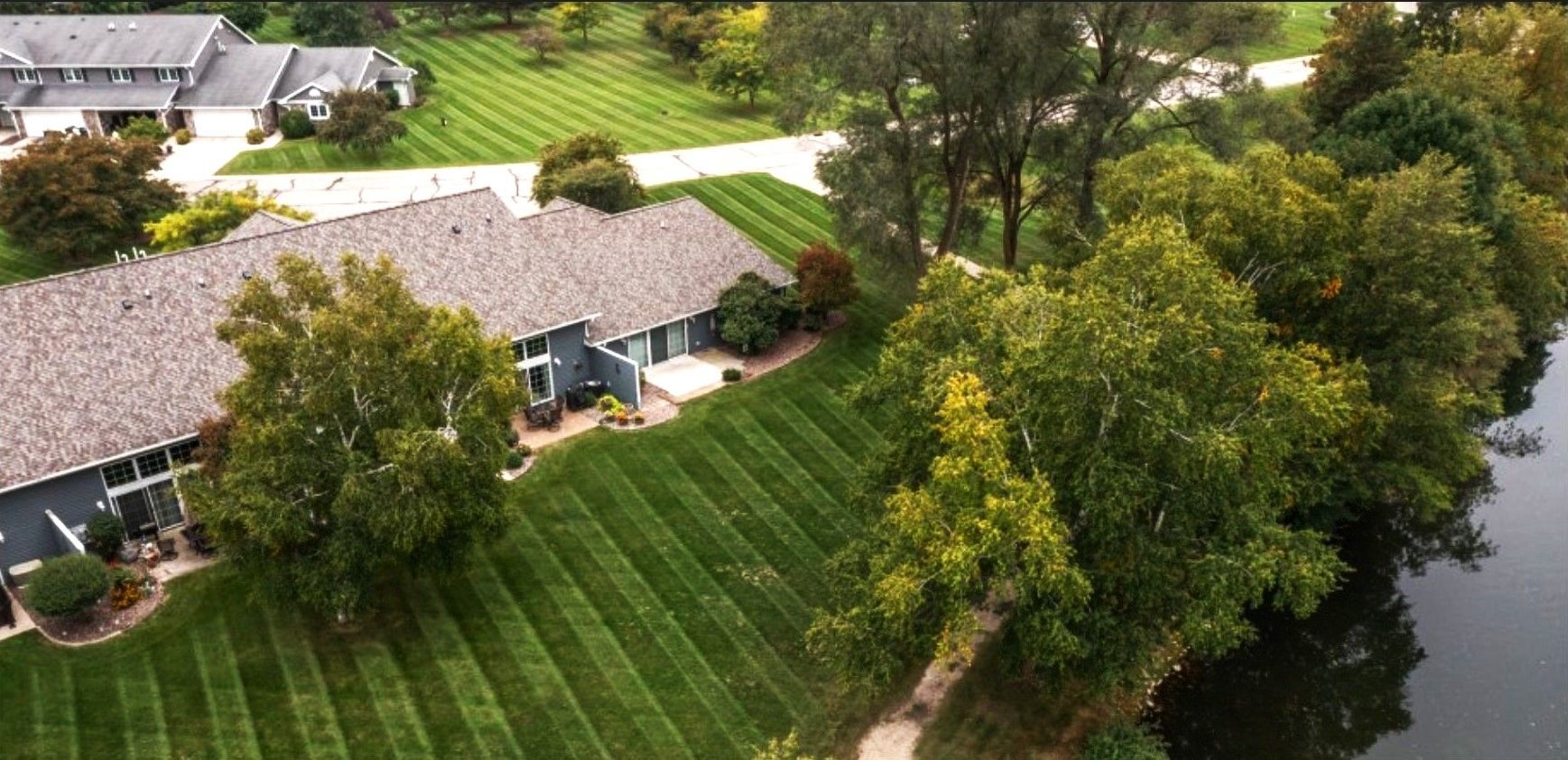 Freshly mowed green lawn beside a paved path, lined with trees under a bright blue sky