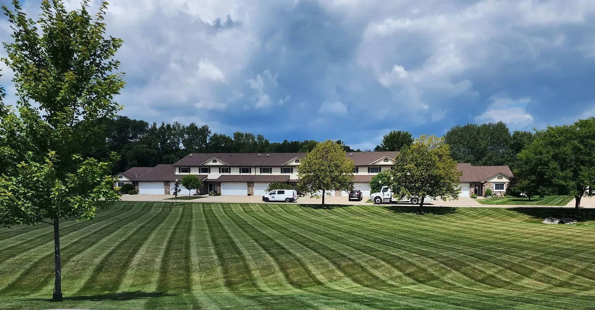 Wide mowed lawn leading to a white building with trees under a cloudy sky