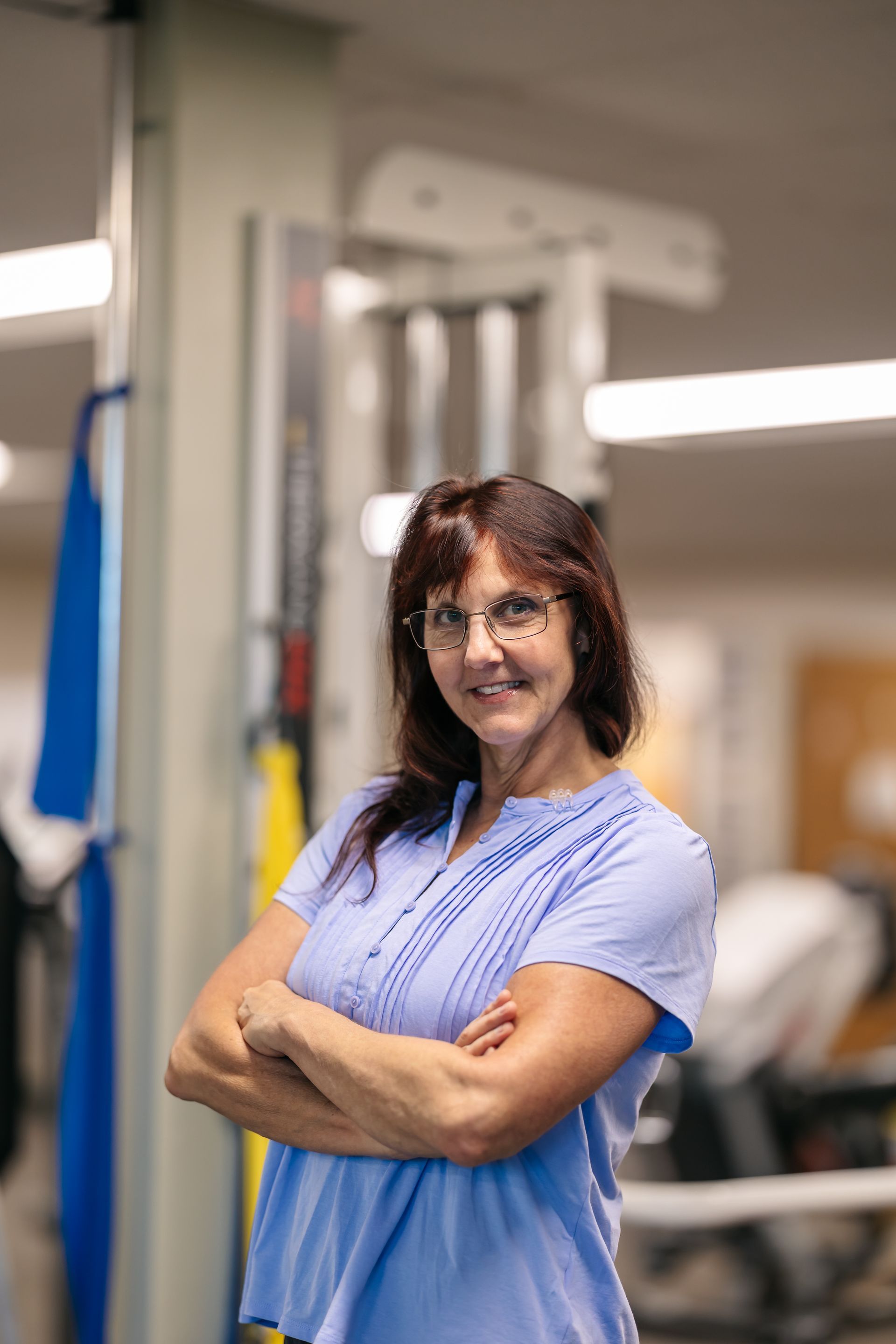 Person in blue scrubs standing with arms crossed in a gym or rehab setting