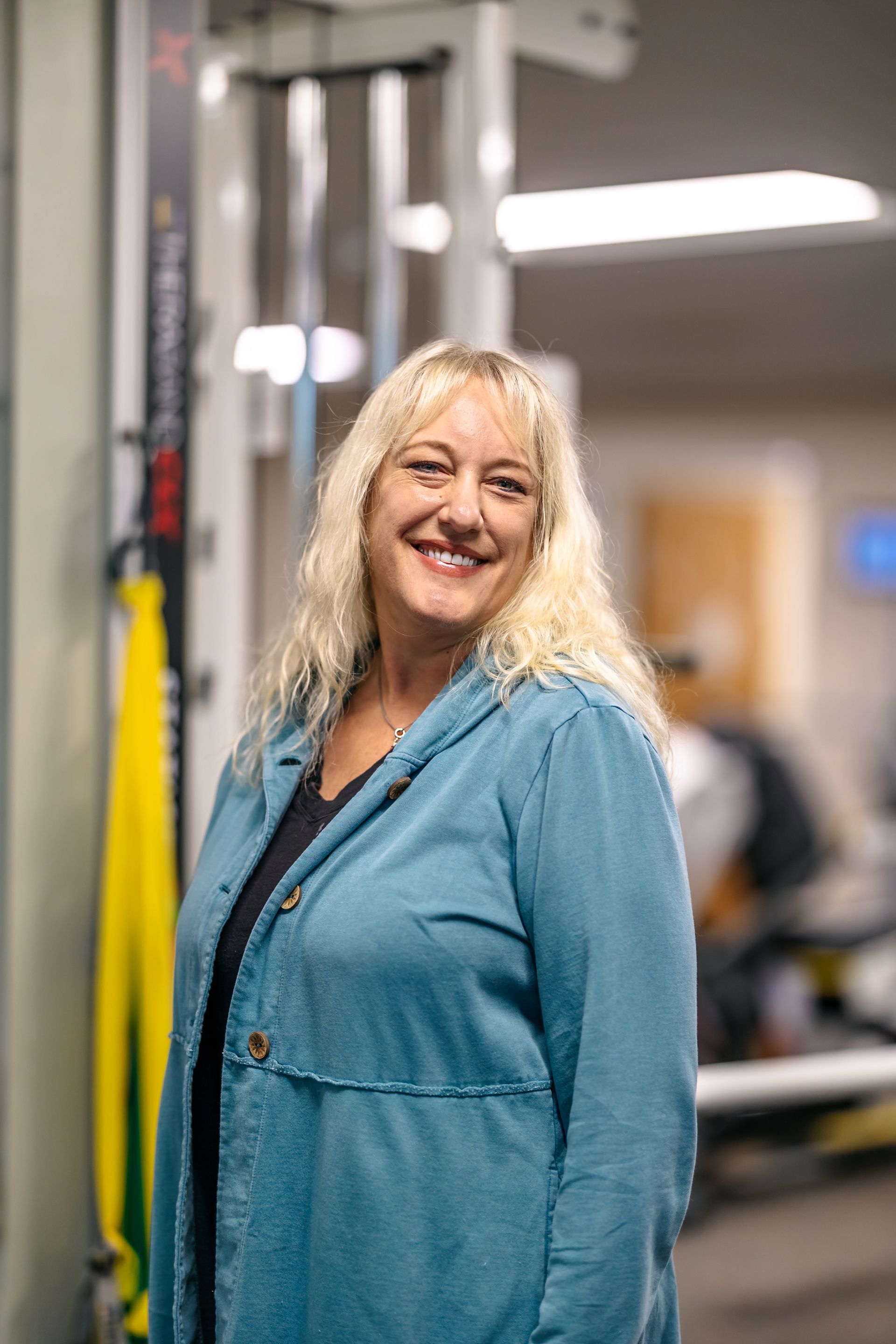 Smiling woman in a teal shirt standing in a gym or fitness facility
