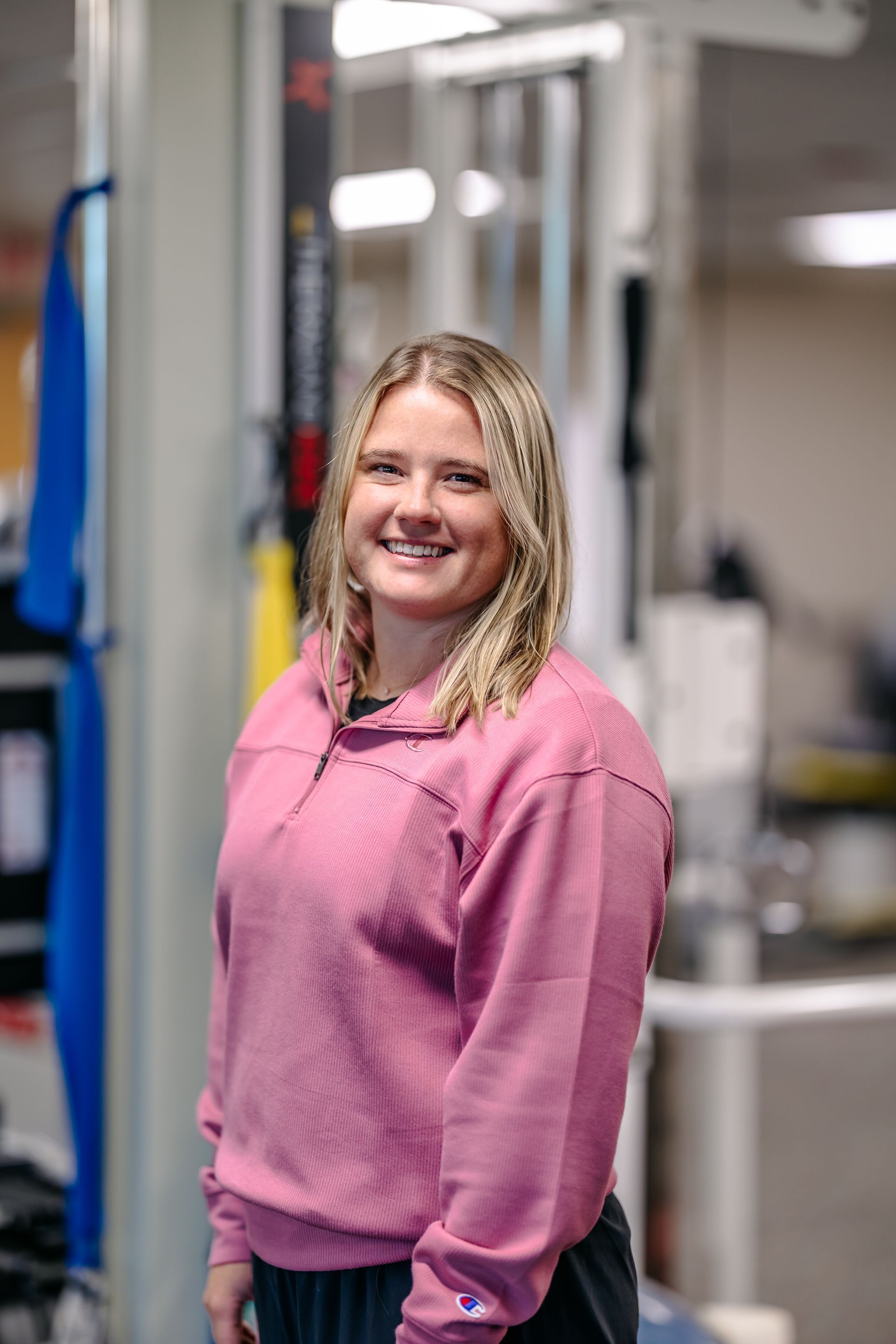 Smiling person in a pink sweater standing in an industrial workspace