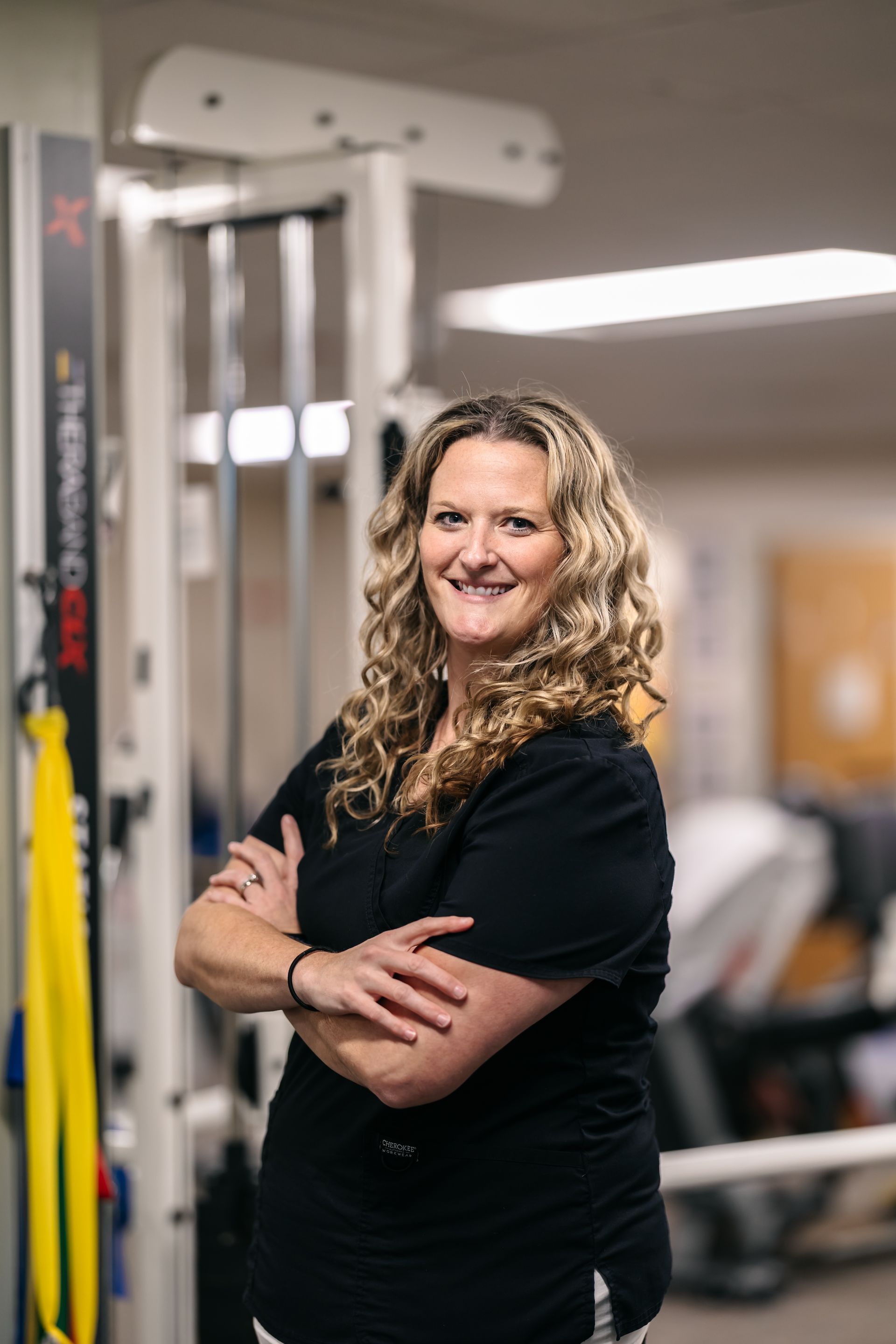 Smiling woman in black shirt standing with arms crossed in a gym.