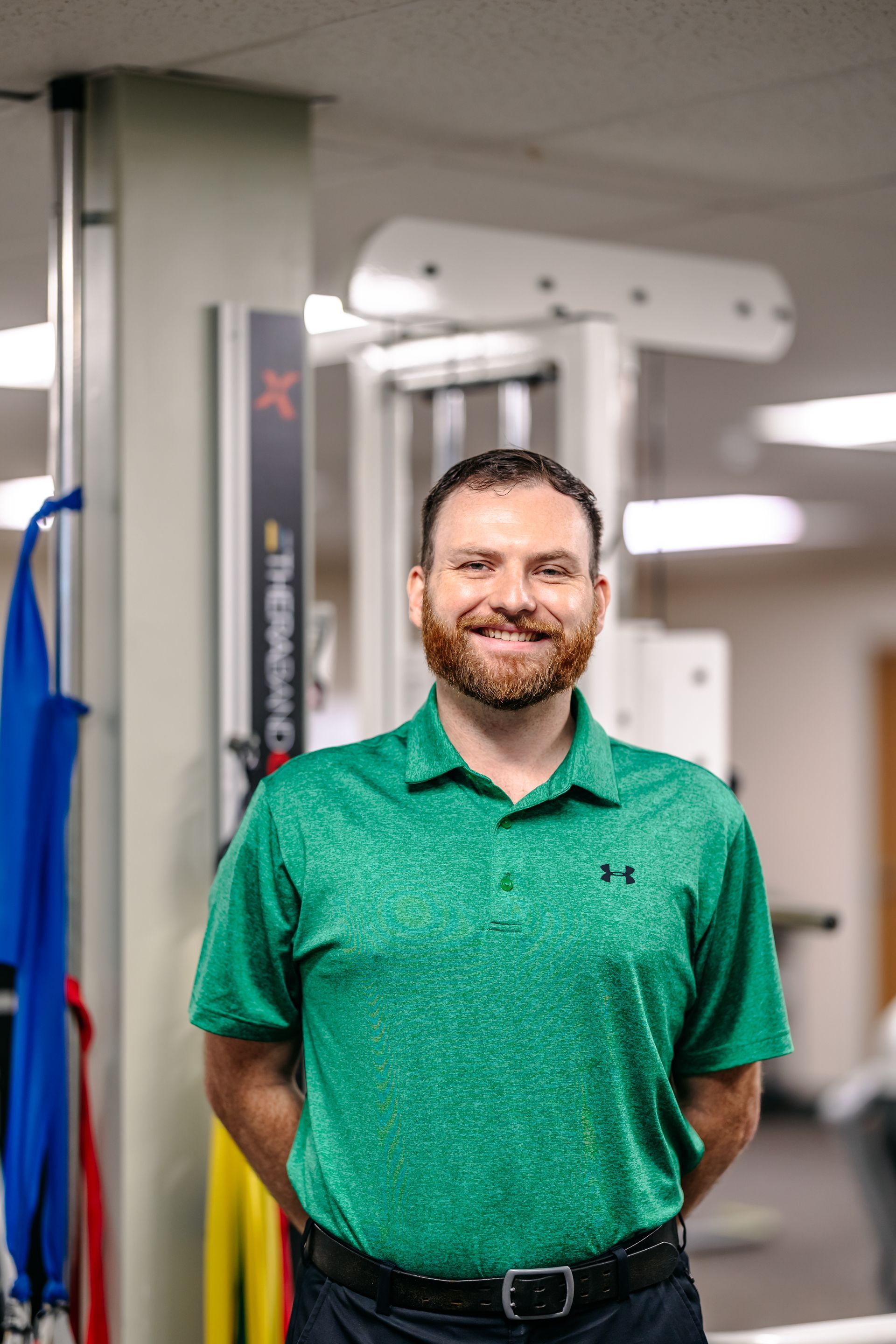 Smiling man in a green polo shirt standing in a gym near exercise equipment