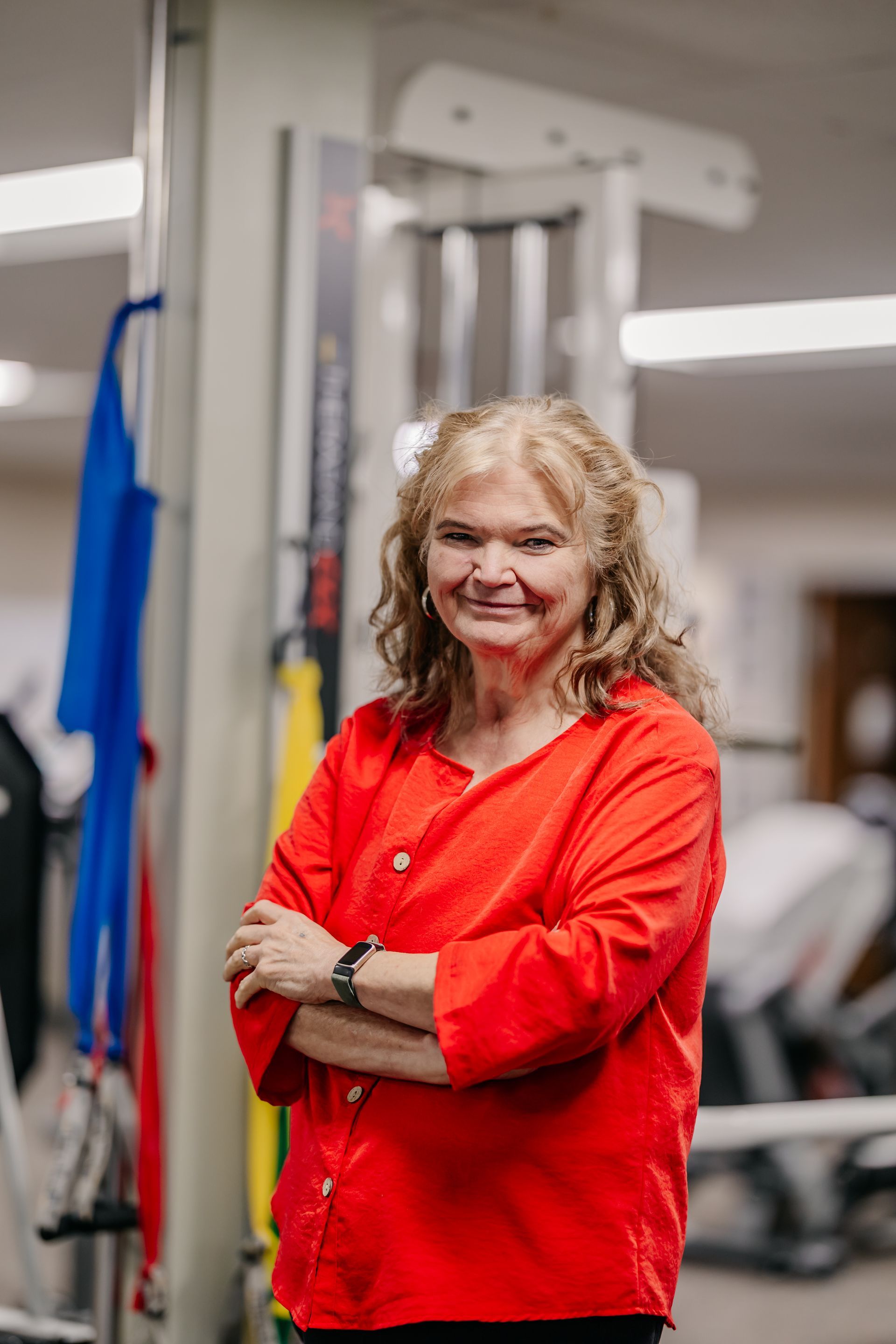Woman in a red shirt standing with arms crossed in a gym setting