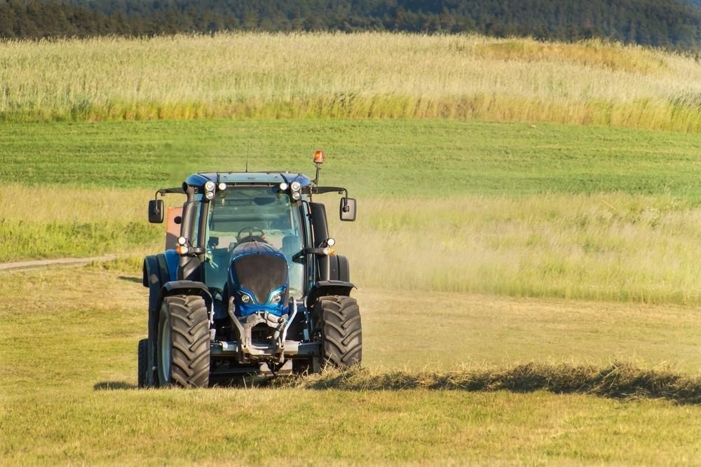 A Blue Tractor Is Driving Through A Grassy Field — JBS Mobile In Richmond Hill, NSW