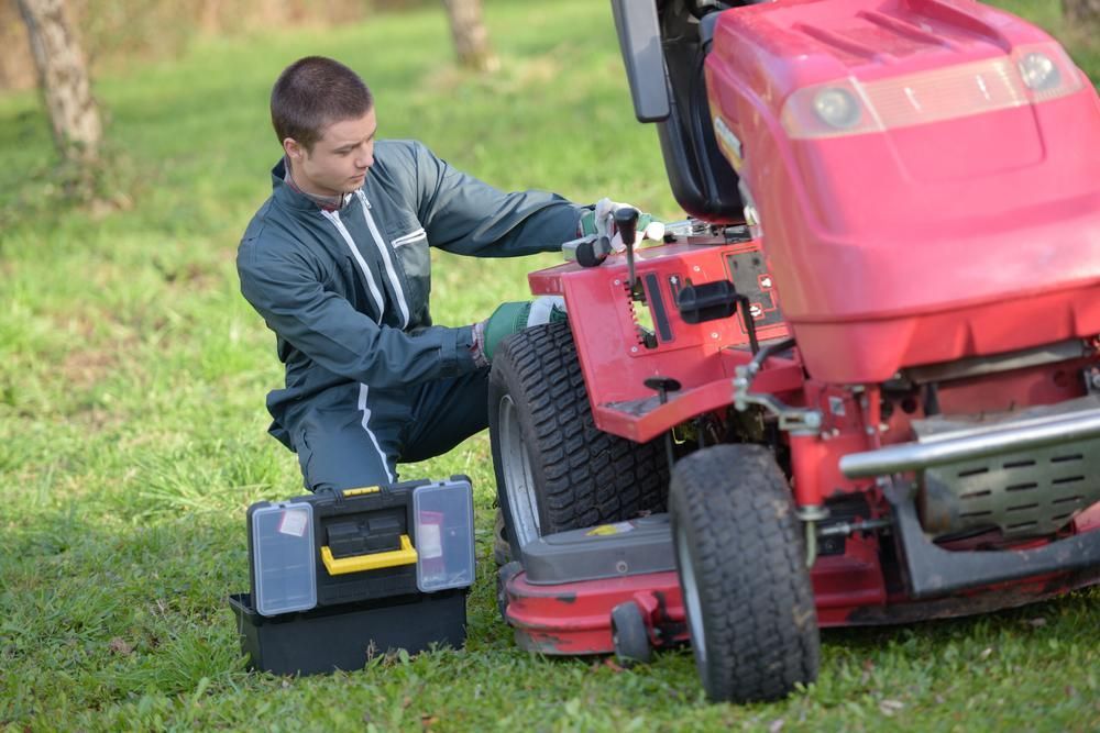 A Man Is Kneeling Down Next To A Lawn Mower — JBS Mobile In Lennox Head, NSW
