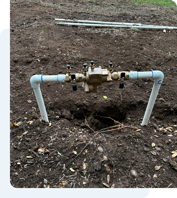 A water meter is sitting in the dirt next to a pipe.
