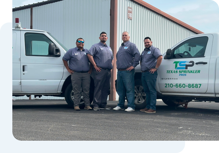 A team of men posing for a picture in front of Texas Sprinkler Pro's trucks.