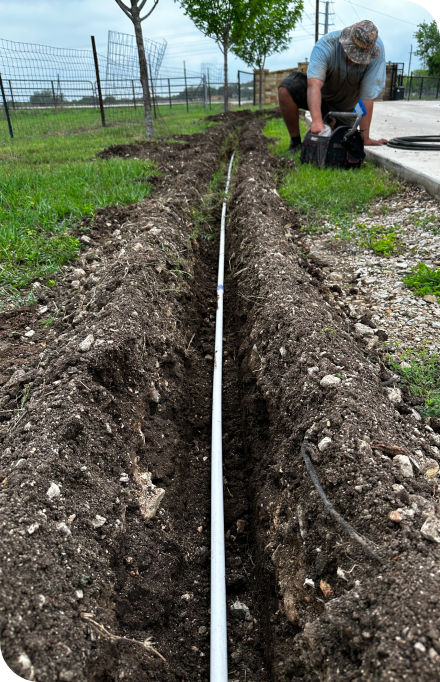 A man is working on a pipe in the dirt doing water sprinkler system repairs.