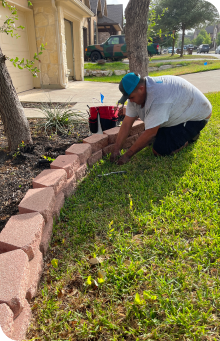 A man is kneeling down in the grass doing water sprinkler system maintenance.