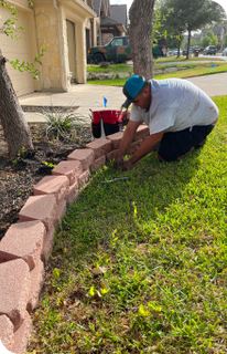 A man is kneeling down in the grass doing water sprinkler system maintenance in San Antonio, TX.