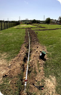 A hose is laying in the middle of a grassy field for a water conservation sprinkler system.