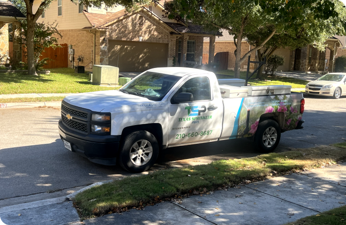 A white truck with Texas Sprinkler Pro's written on the side is parked in front of a happy customers lawn.