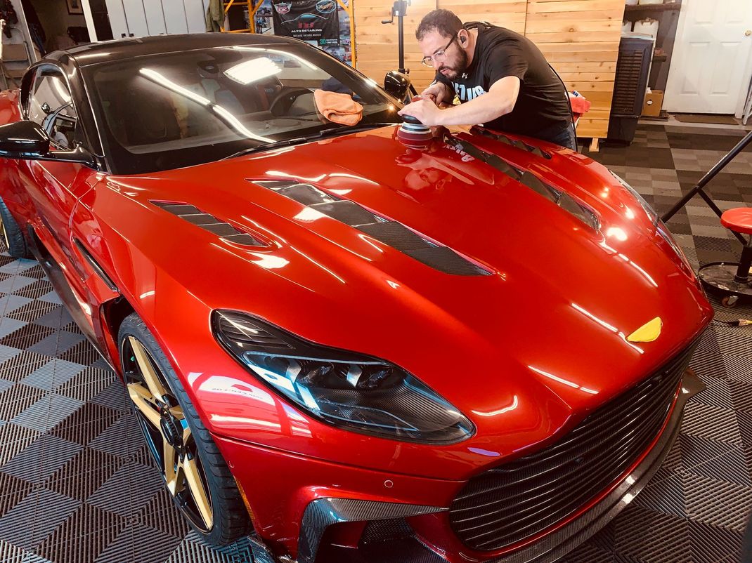 Man detailing a red Aston Martin in a garage.