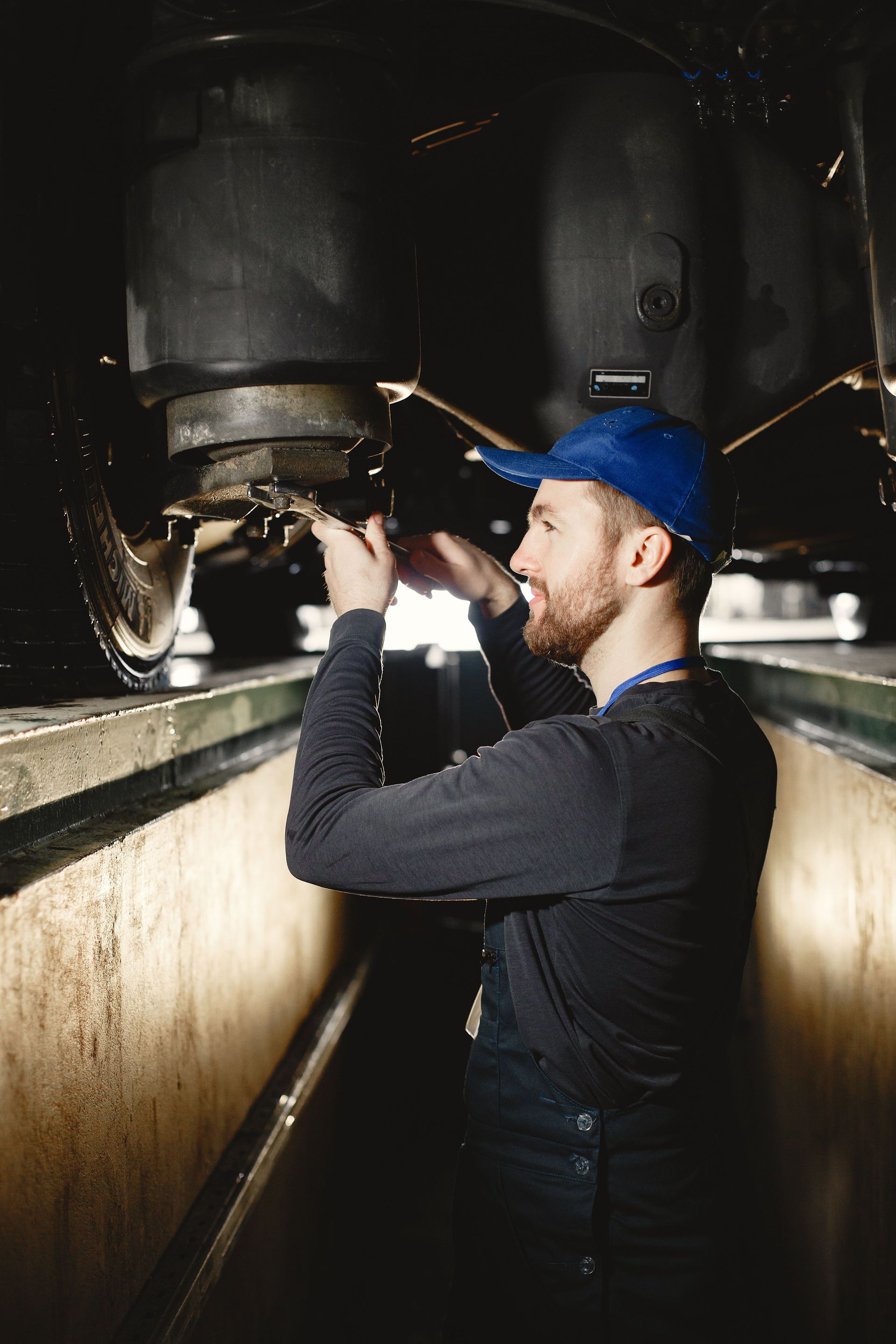 Worker inspecting machinery in a narrow industrial trench, wearing a blue cap and black shirt. | HD Auto Care and More