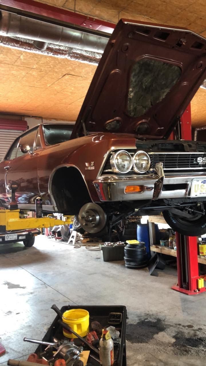 Brown classic car lifted on a garage hoist with hood open, showing the front end during repair.