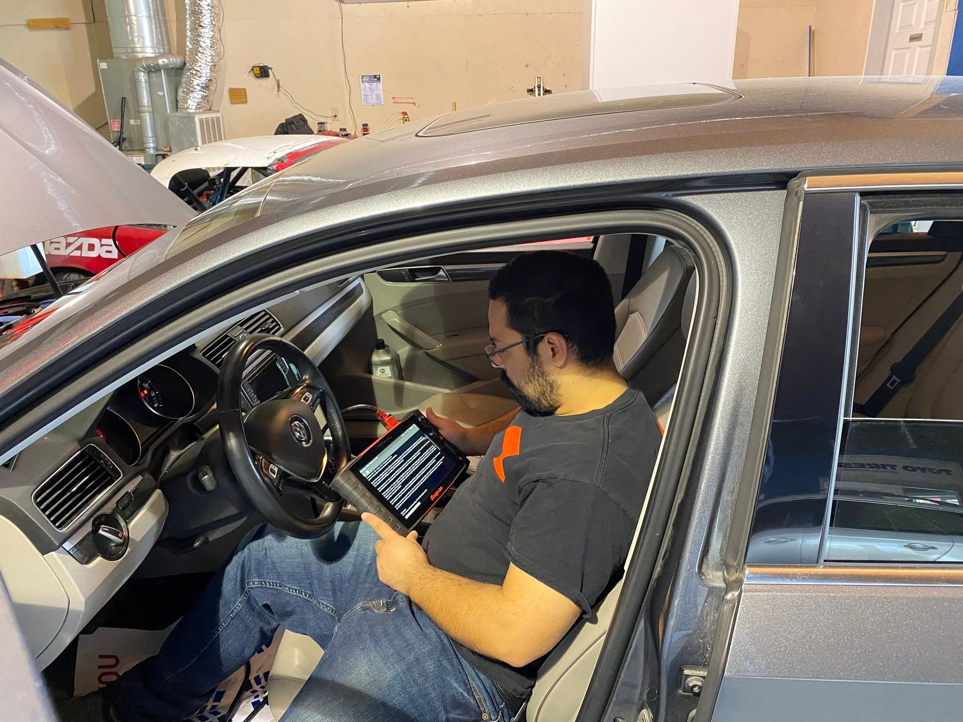 Man sitting in a gray car garage, looking at a tablet inside the driver’s seat