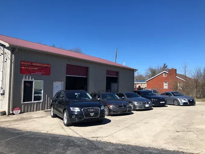 Black sedan and several cars parked outside a small auto shop on a sunny day