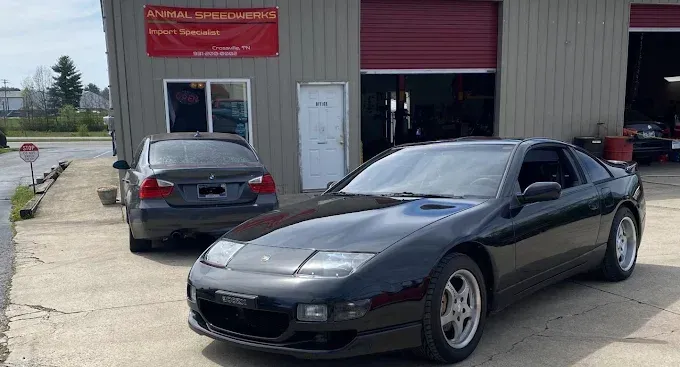 Two black sports cars parked outside a garage with an open bay door