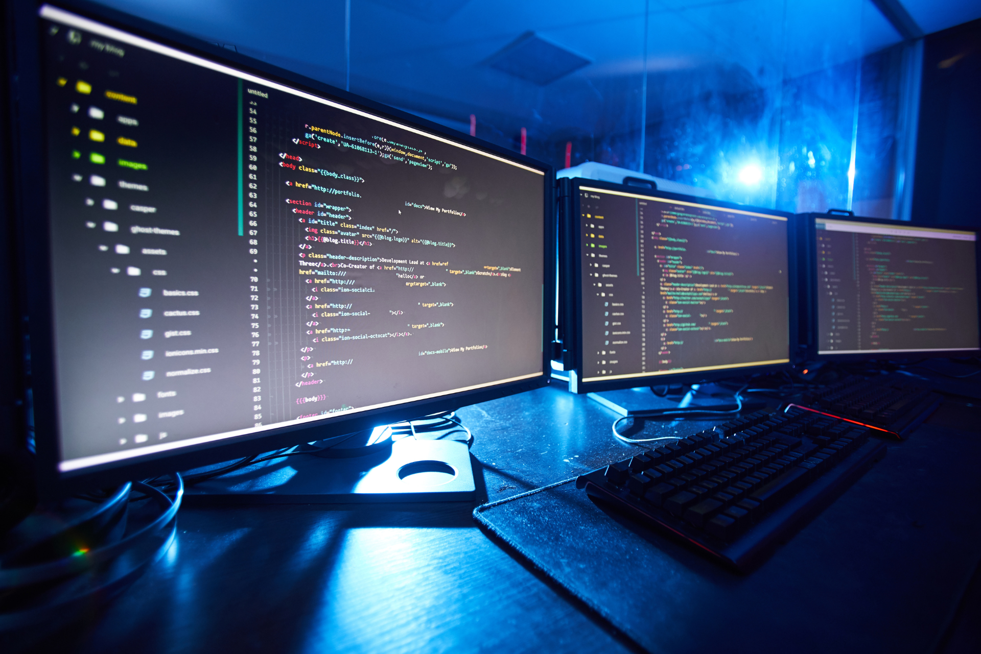 Tres monitores de computadora están sobre un escritorio con un teclado.