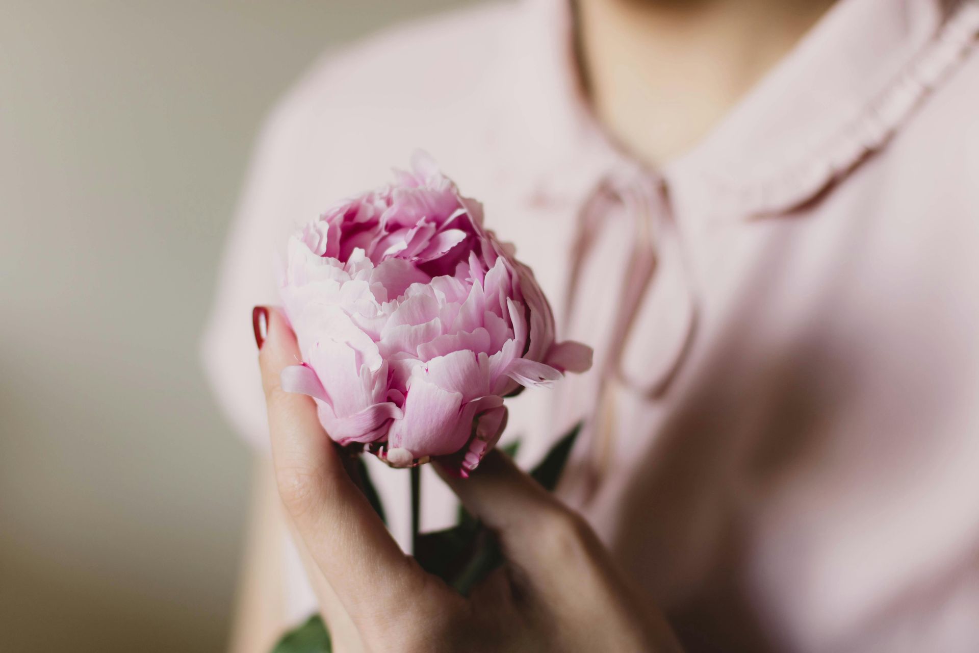 Uma mulher de camisa rosa está segurando uma flor rosa