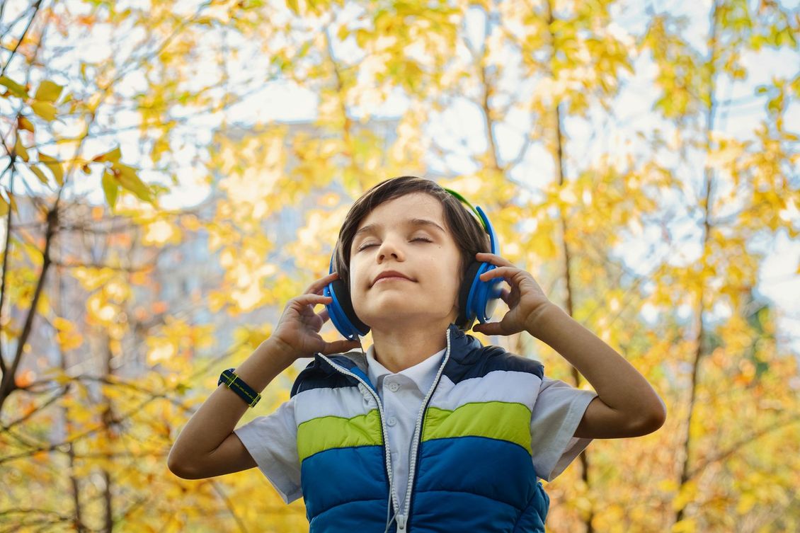 Um menino usando fones de ouvido está ouvindo música em um parque.