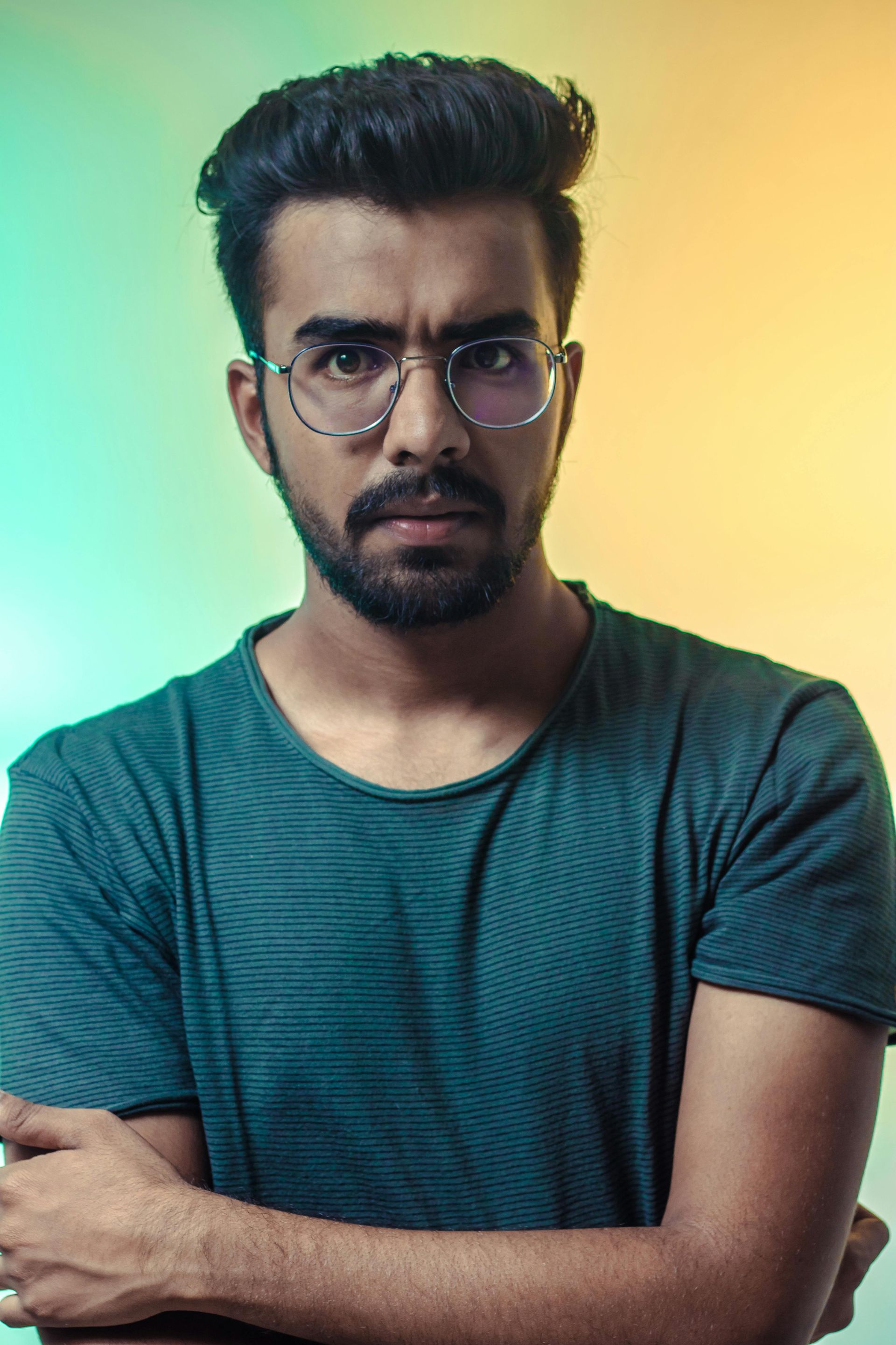 Um homem de óculos e barba está de pé com os braços cruzados.