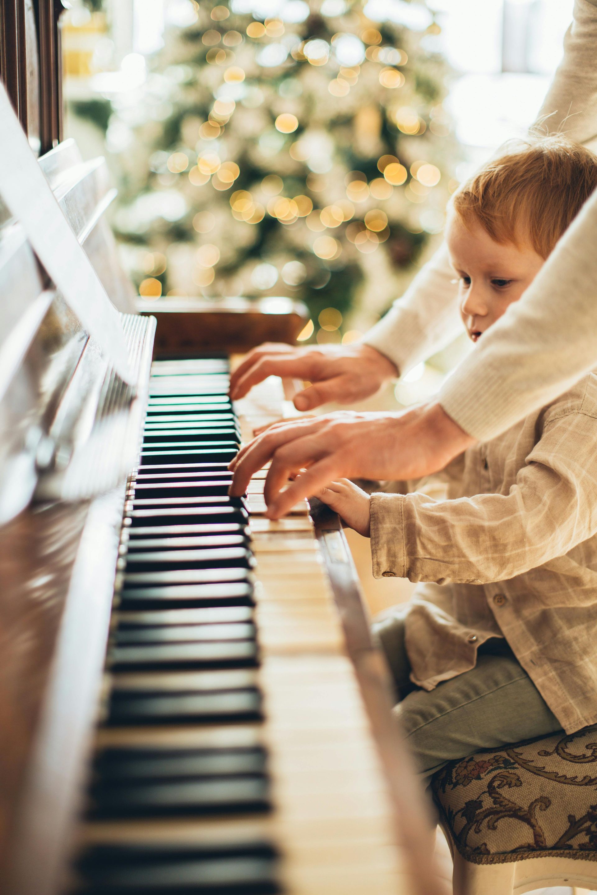Um garotinho está tocando piano em frente a uma árvore de natal.