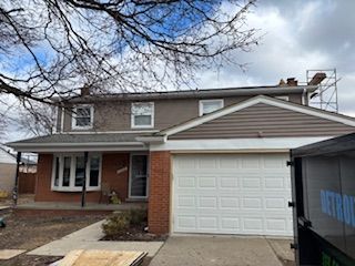 Two-story suburban house with brick front, white garage, and leafless trees overhead