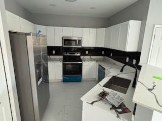 Modern white kitchen with stainless steel appliances, black backsplash, and a cluttered countertop