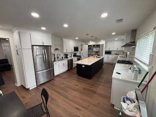 Bright modern kitchen with white cabinets, stainless steel fridge, and dark wood floors