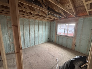 Bare unfinished room under construction with exposed wooden framing, insulation, and a window.