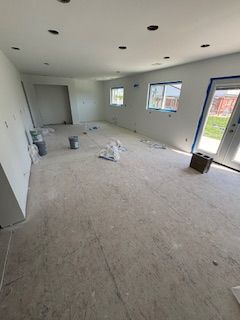 Empty unfinished room with white walls, carpet, recessed lights, and large windows and sliding glass door.