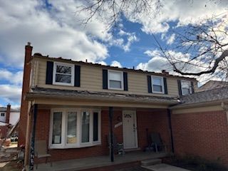 Two-story brick house with a covered front porch under a partly cloudy sky