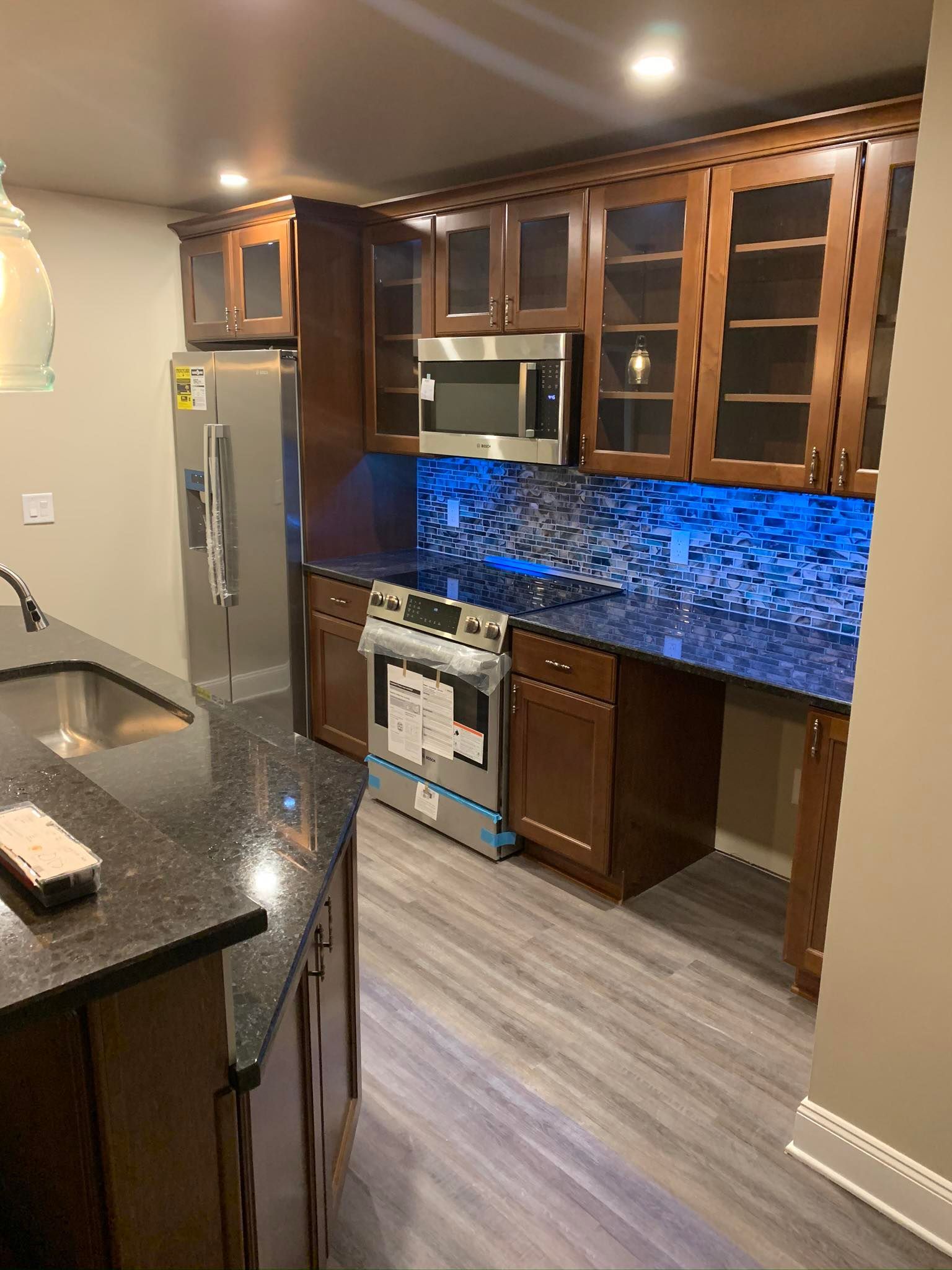 Modern kitchen with dark cabinets, stainless appliances, granite counters, and blue tile backsplash