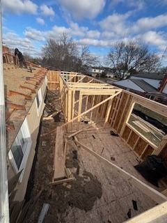 House roof under construction with exposed wooden framing under a cloudy blue sky