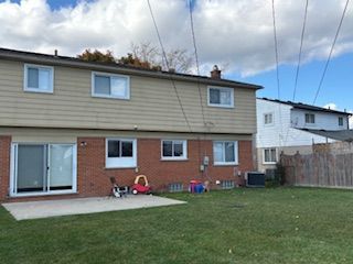Suburban townhouse with brick lower level, beige siding, patio, and grassy backyard under a cloudy sky