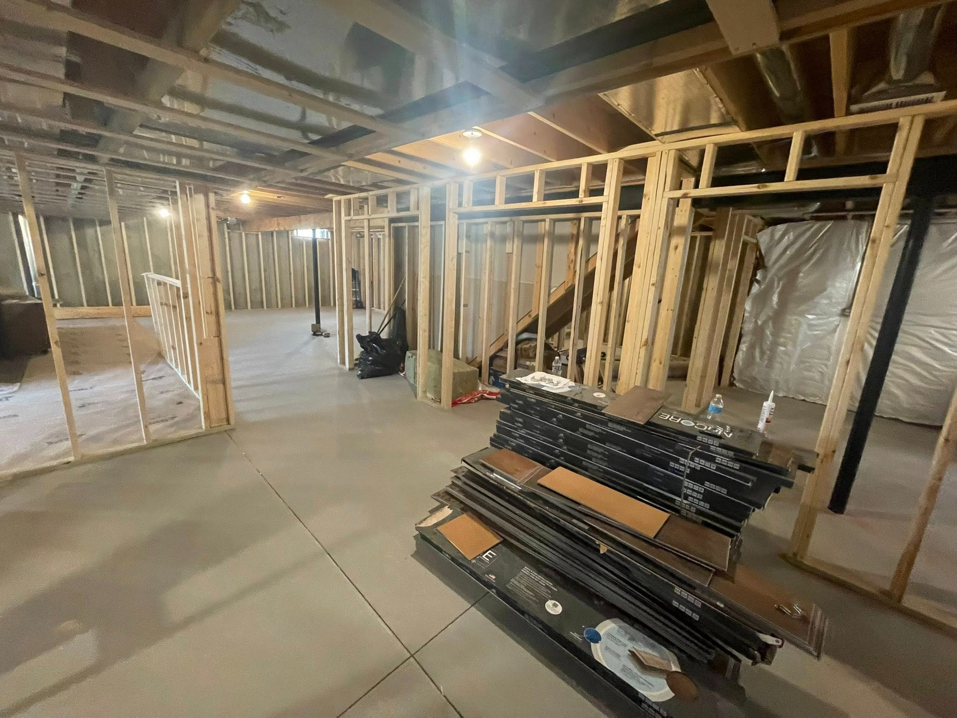 Unfinished basement under construction with exposed framing, concrete floor, and stacked building materials.