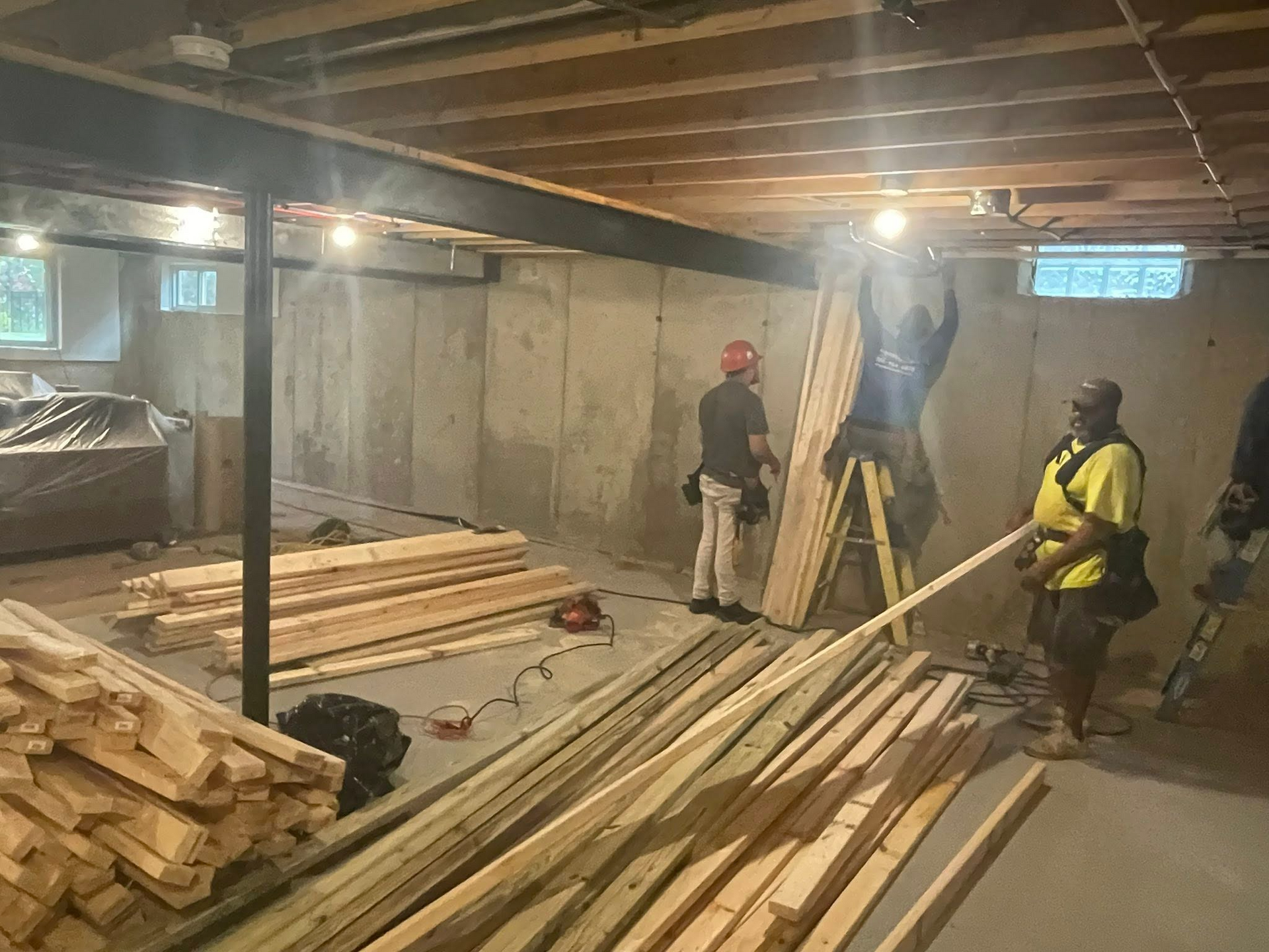 Workers in a dim construction site with lumber stacks and exposed beams