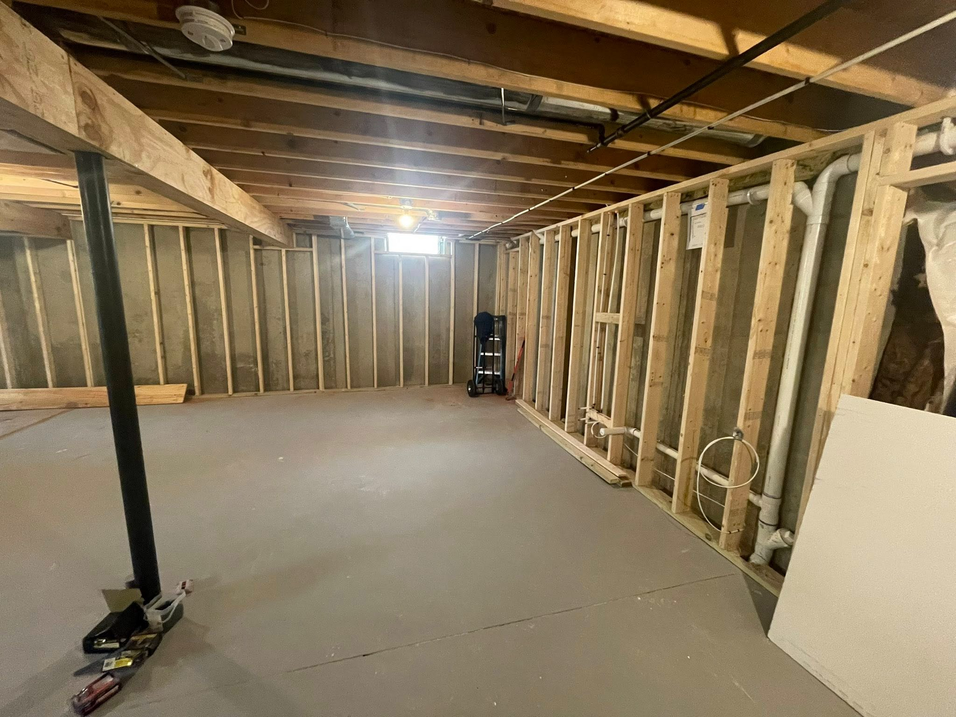 Unfinished basement with exposed framing, concrete floor, and construction materials near the walls.
