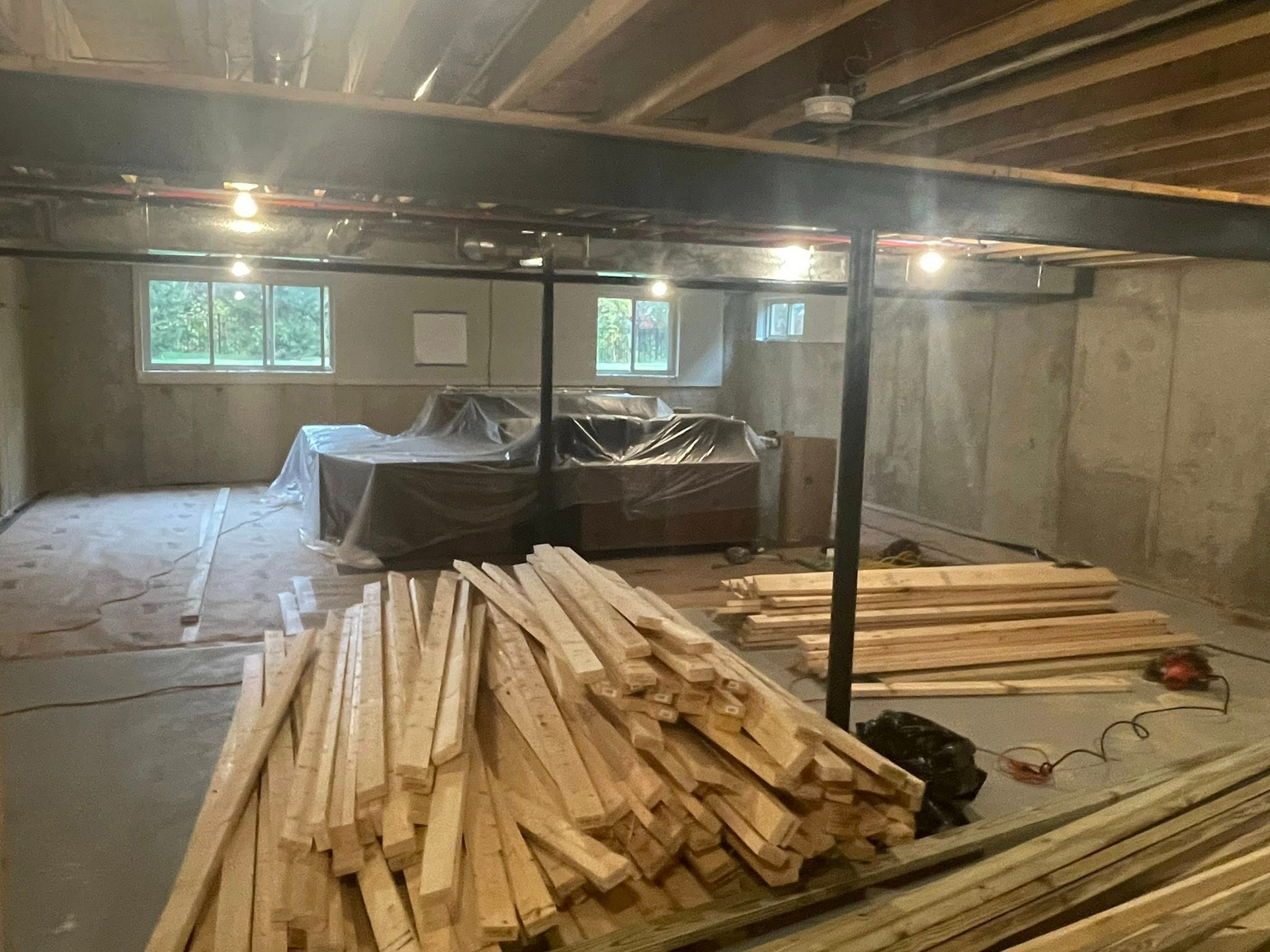 Basement with stacked lumber, concrete walls, and covered equipment under low beams