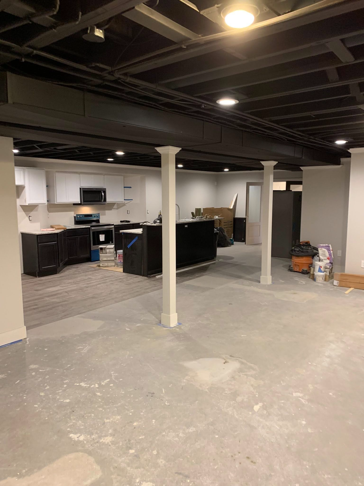 Partially finished basement with concrete floor, exposed ceiling, white support columns, and a small office area.