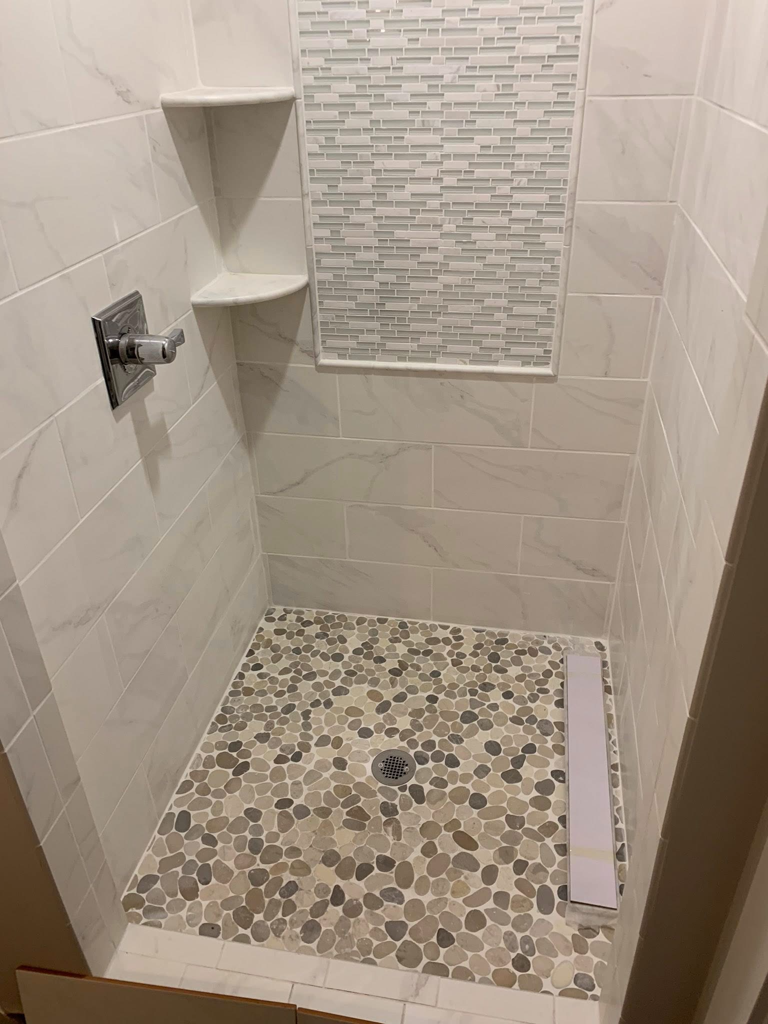 Empty tiled shower stall with mosaic floor, wall shelves, and a shower valve.