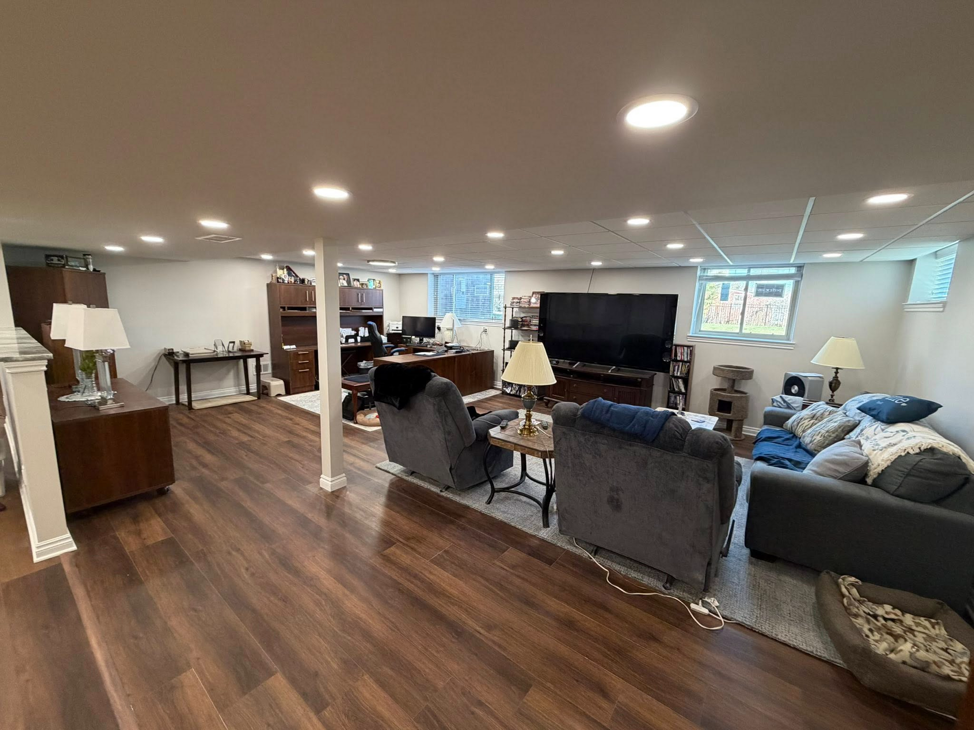Spacious basement living area with dark wood floors, seating, TV, and bright recessed lighting