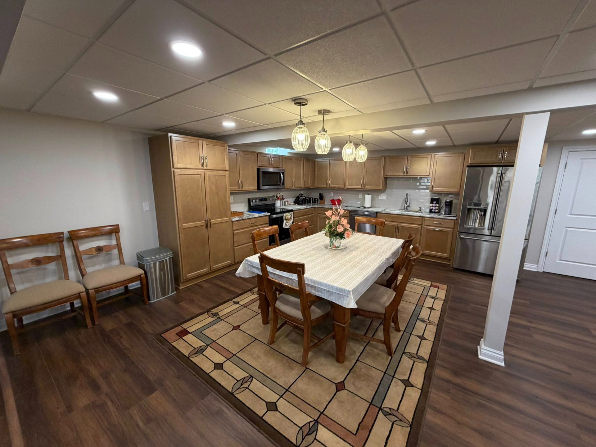Open kitchen and dining area with wooden table, chairs, rug, and stainless steel appliances