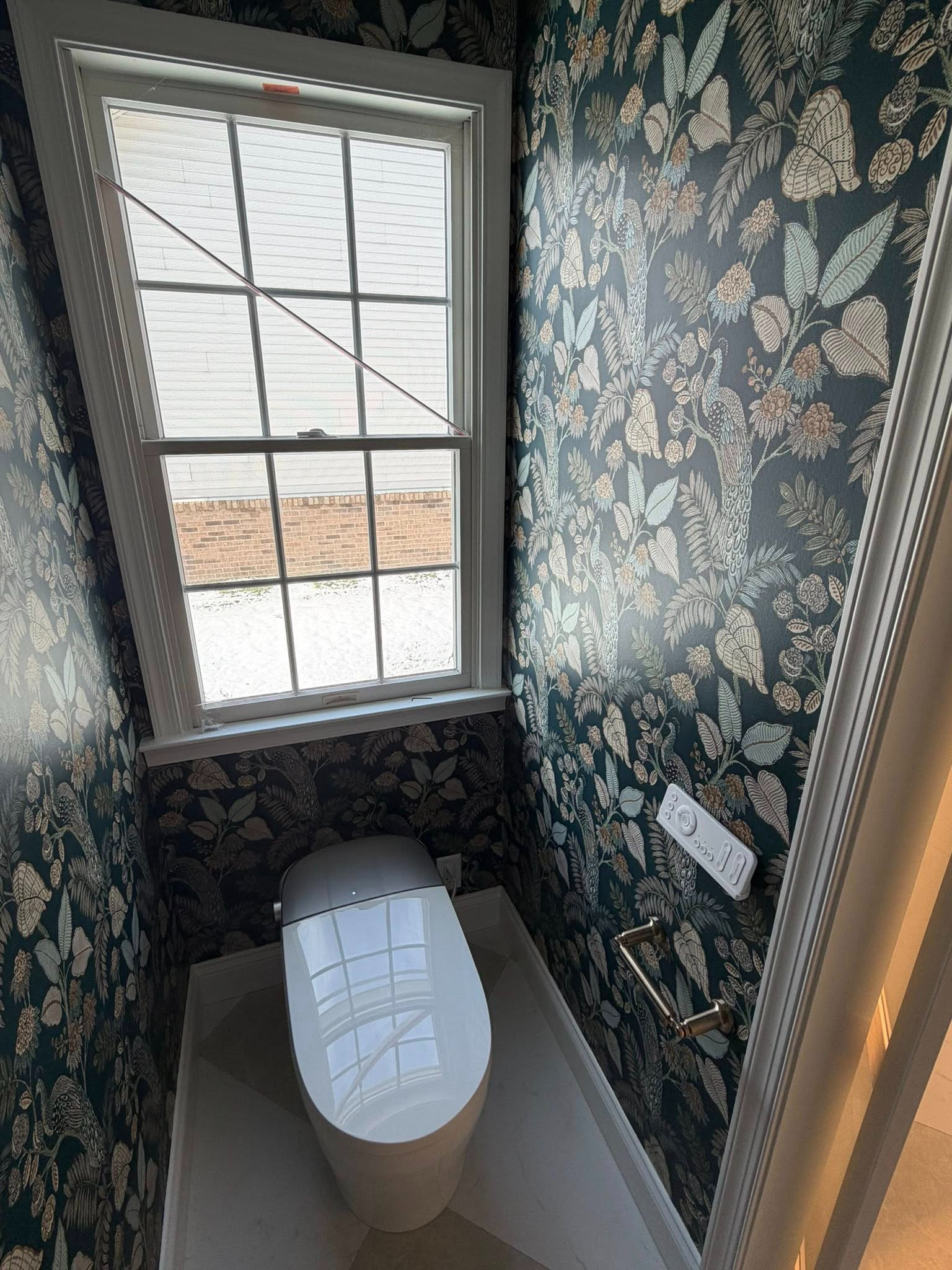 Small bathroom with floral wallpaper, window, and toilet viewed from above.