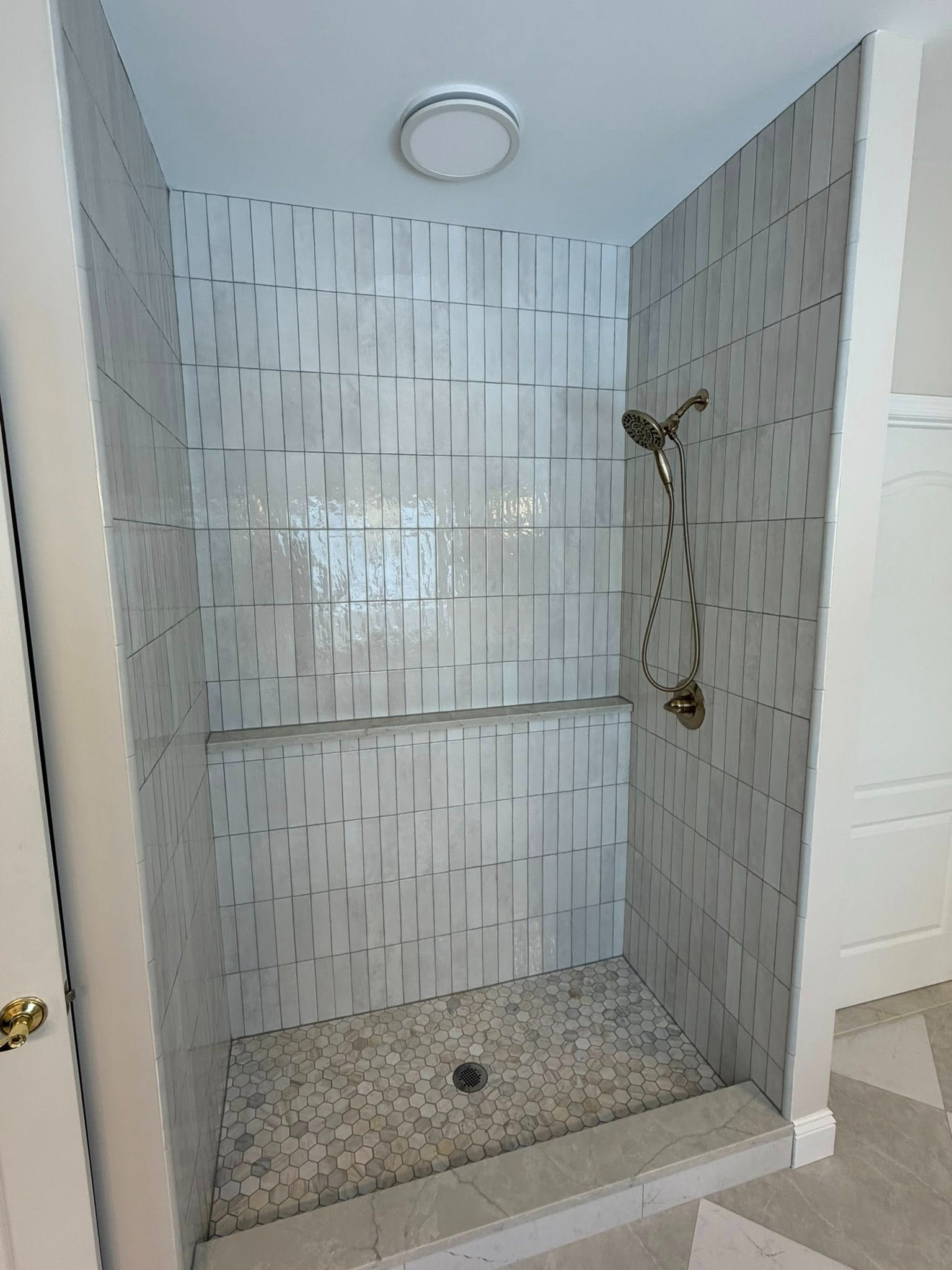 Small tiled shower stall with built-in niche and handheld showerhead.
