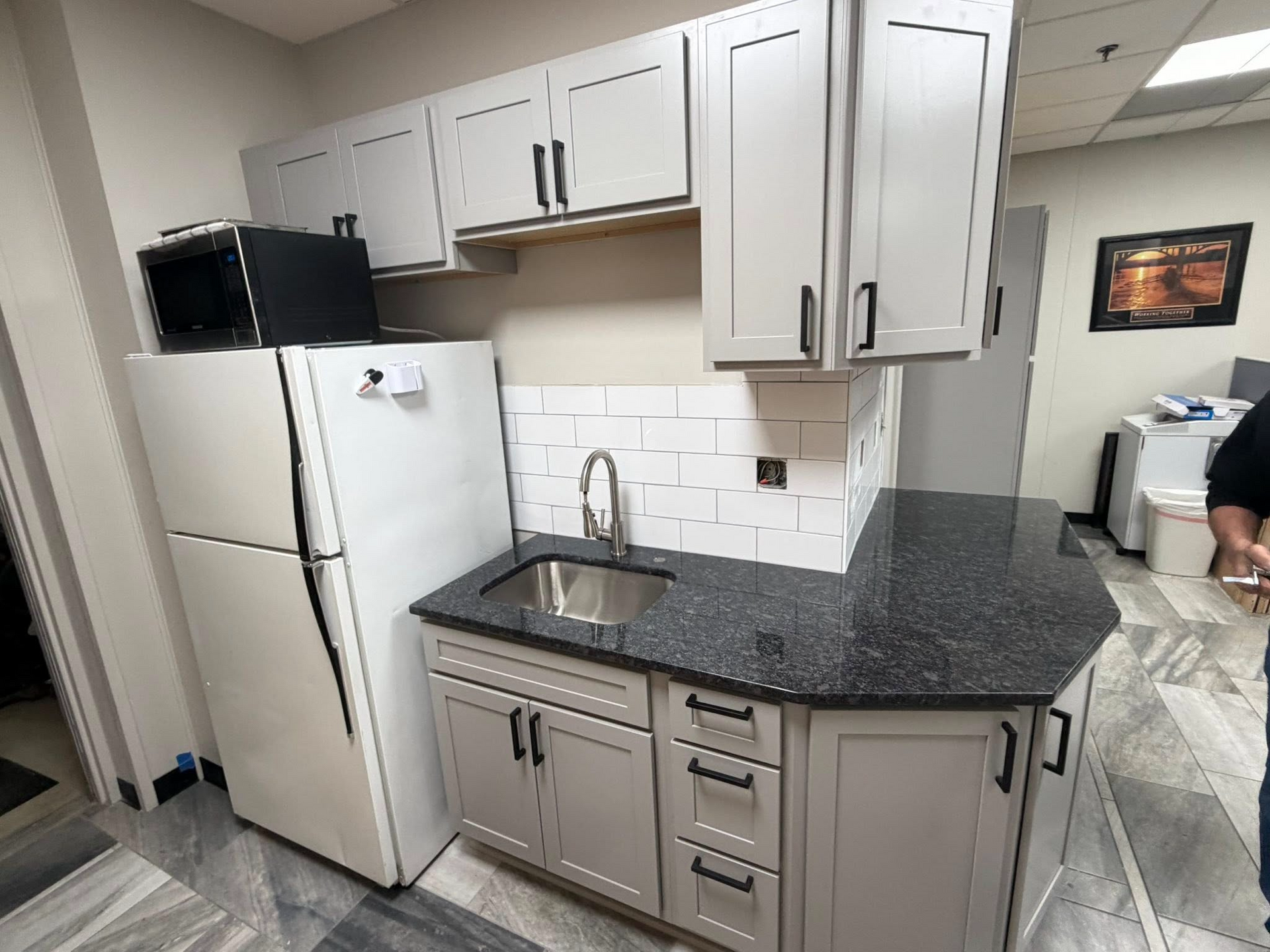 Small kitchen with white cabinets, stainless fridge, dark granite counter, and a sink backsplash.