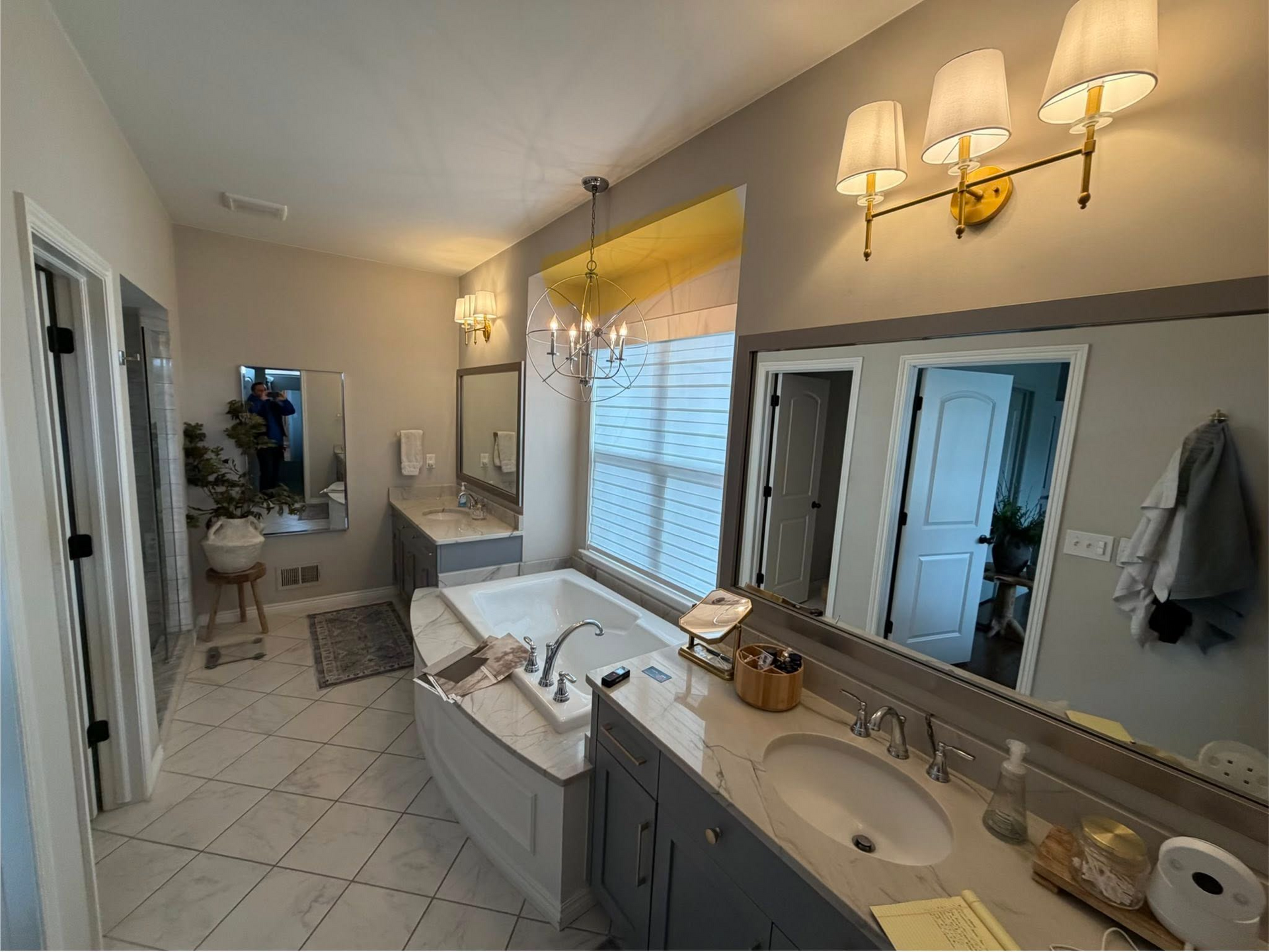 Bright bathroom with double vanity, large mirror, tiled floor, and a soaking tub by a window.