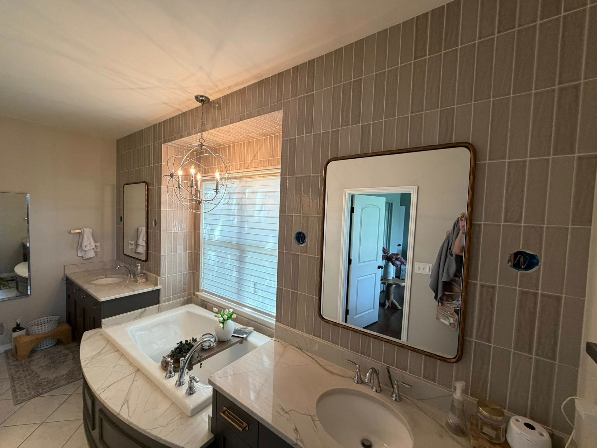 Bathroom with tiled walls, double sinks, mirror, and a window with blinds and lights on the left